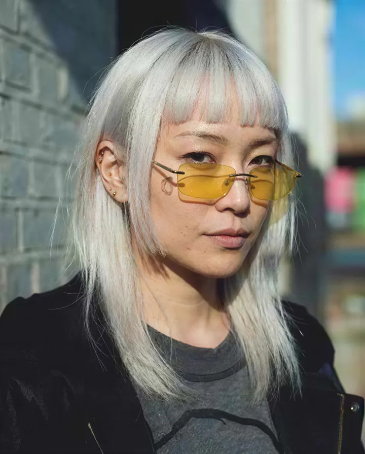 A low-resolution portrait gains clean platinum hair strands and clear tinted glasses.